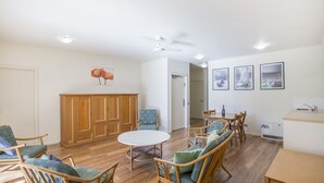 A spacious living area with a round table, wicker chairs, a wooden cabinet, and a ceiling fan. - Mitchellmook in Mollymook (Mollymook Beach)