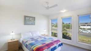 A bedroom with a bed, two bedside tables with lamps, a ceiling fan, and large windows offering a view of the outside. - FREE NIGHT. Pay for 2 stay for 3 (Mollymook Beach)