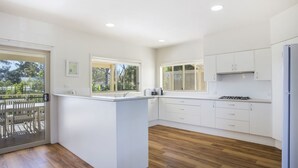 A modern kitchen with white cabinets, a central island, and a view of the outdoors. - Mitchellmook in Mollymook (Mollymook Beach)