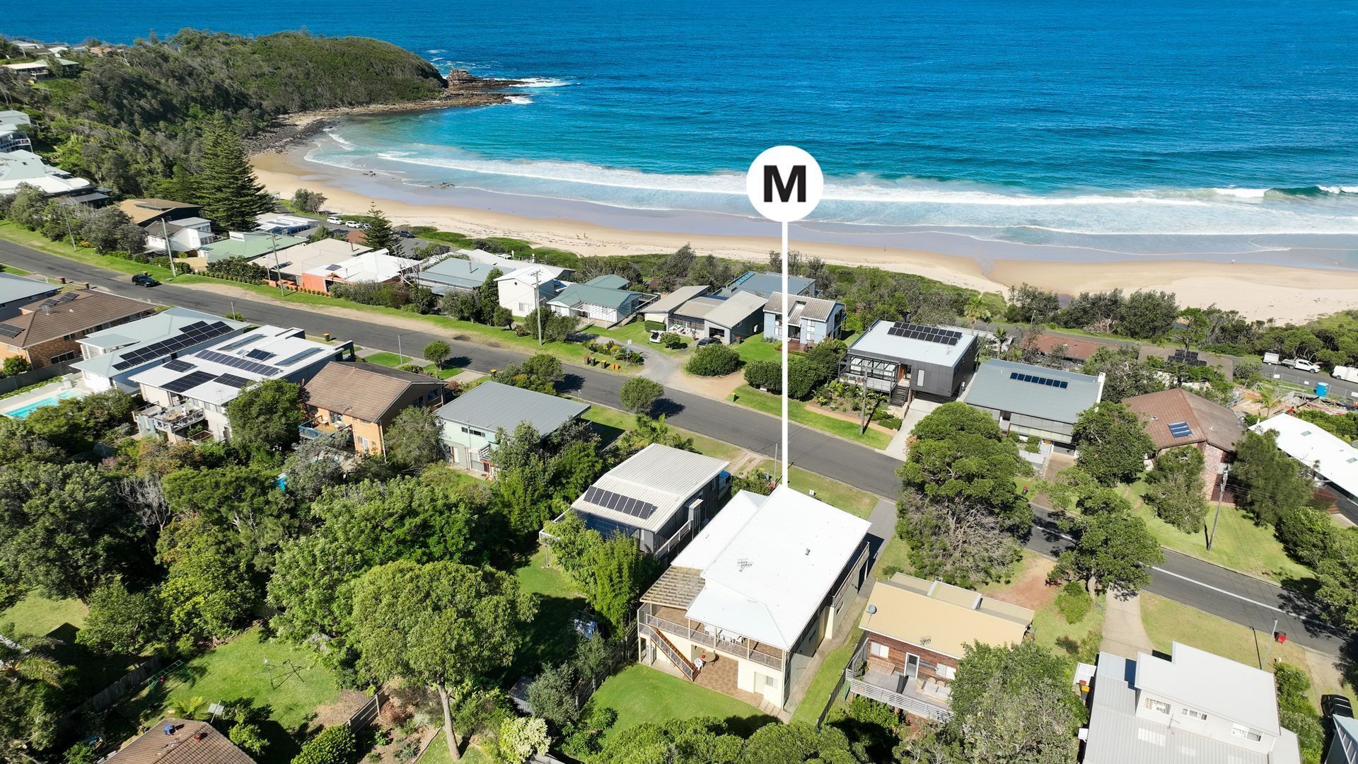 Vue aérienne d’une zone résidentielle côtière, avec des maisons, une plage et une route.