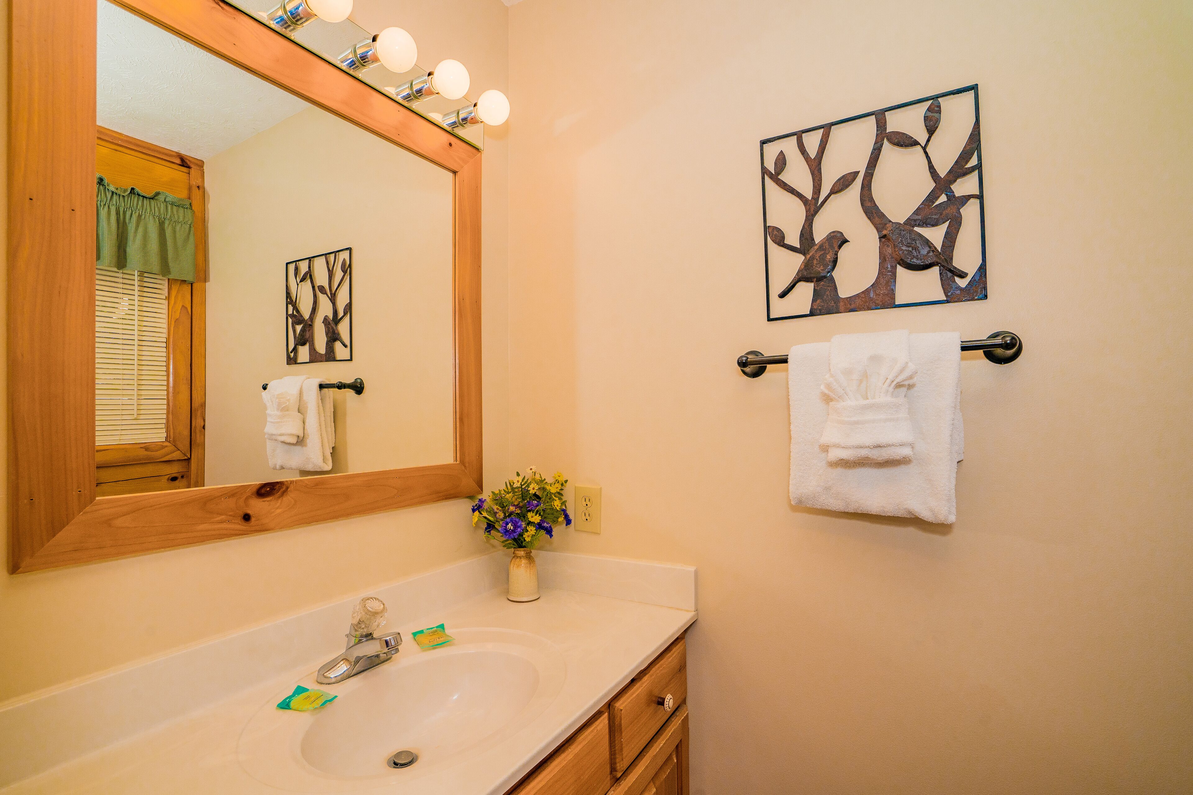 A bathroom with a wooden-framed mirror, a white sink, a vase with flowers, and two wall-mounted towels.