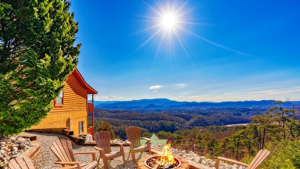 Uma cabana com lareira e cadeiras Adirondack, com vista para uma paisagem montanhosa.