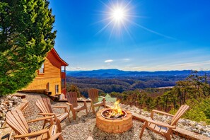 Een chalet met vuurkorf en Adirondack-stoelen met uitzicht op een bergachtig landschap.