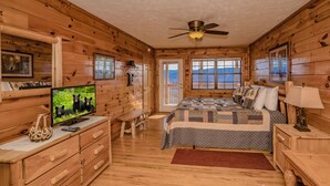 Quarto de cabana de madeira com uma cama, uma televisão, uma escrivaninha e uma janela.
