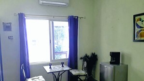 Una habitación pequeña con ventana, una mesa, dos sillas, un refrigerador y una cafetera.