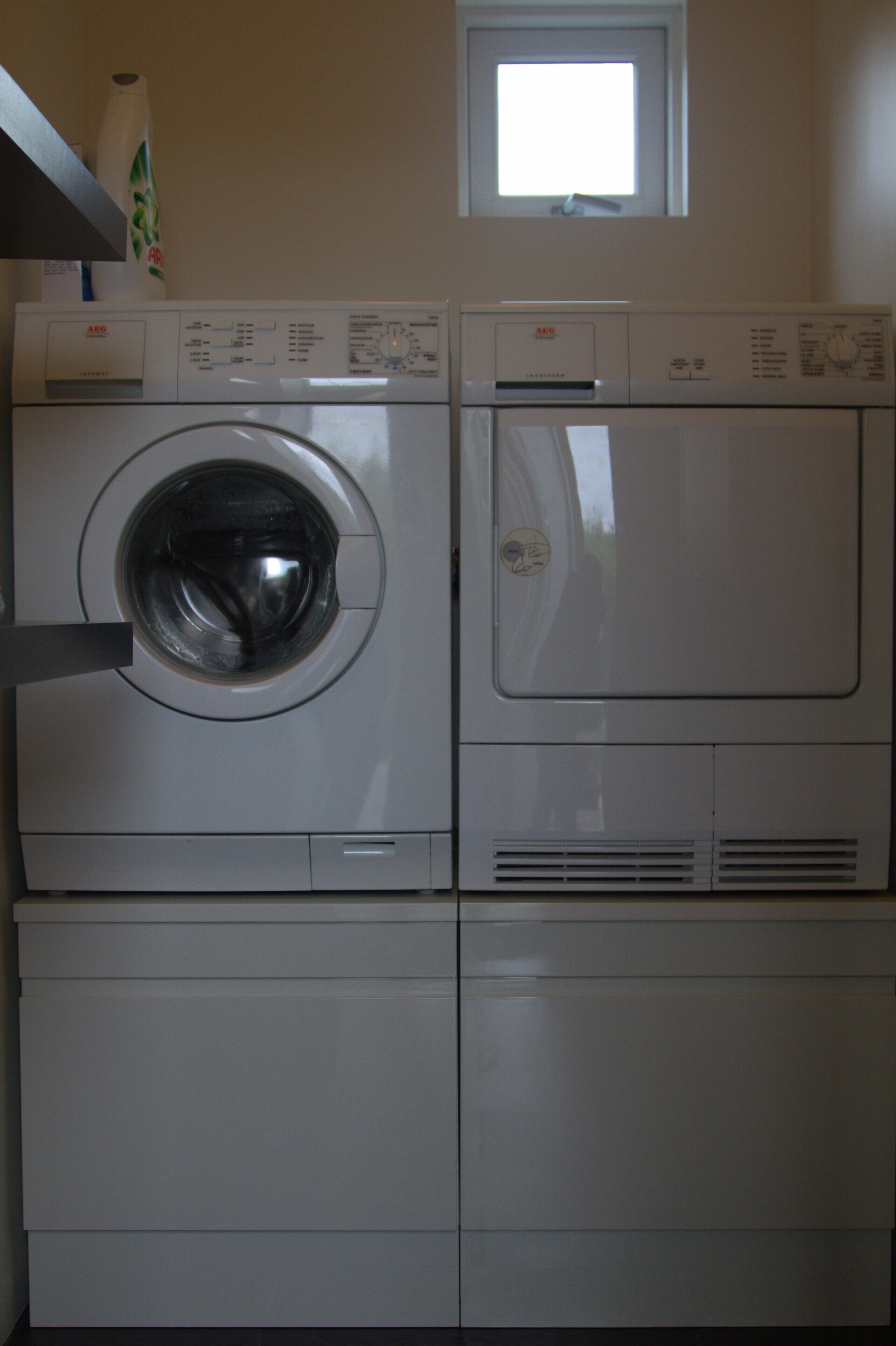 A front-loading washing machine and dryer stacked in a laundry room with a small window above.