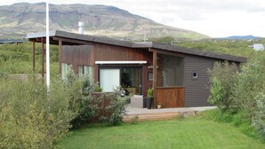 A modern house with a large front porch, a garage, and a view of mountains in the background. - Luxury cottage, Golden  Circle. HG-00004618 (Grímsnes- og Grafningshreppur)