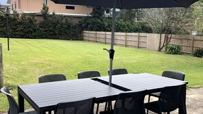 Une terrasse extérieure avec une table et des chaises, un parasol rétractable et une clôture en bois en arrière-plan.