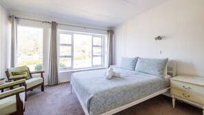 Une chambre à coucher avec un grand lit, une table de chevet, une chaise et une fenêtre avec des rideaux.