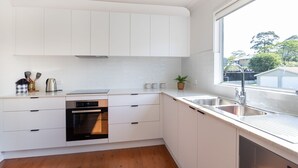 A modern kitchen with white cabinets, a stainless steel sink, and a built-in oven. - Surf & Turf Retreat in Mollymook (Mollymook)