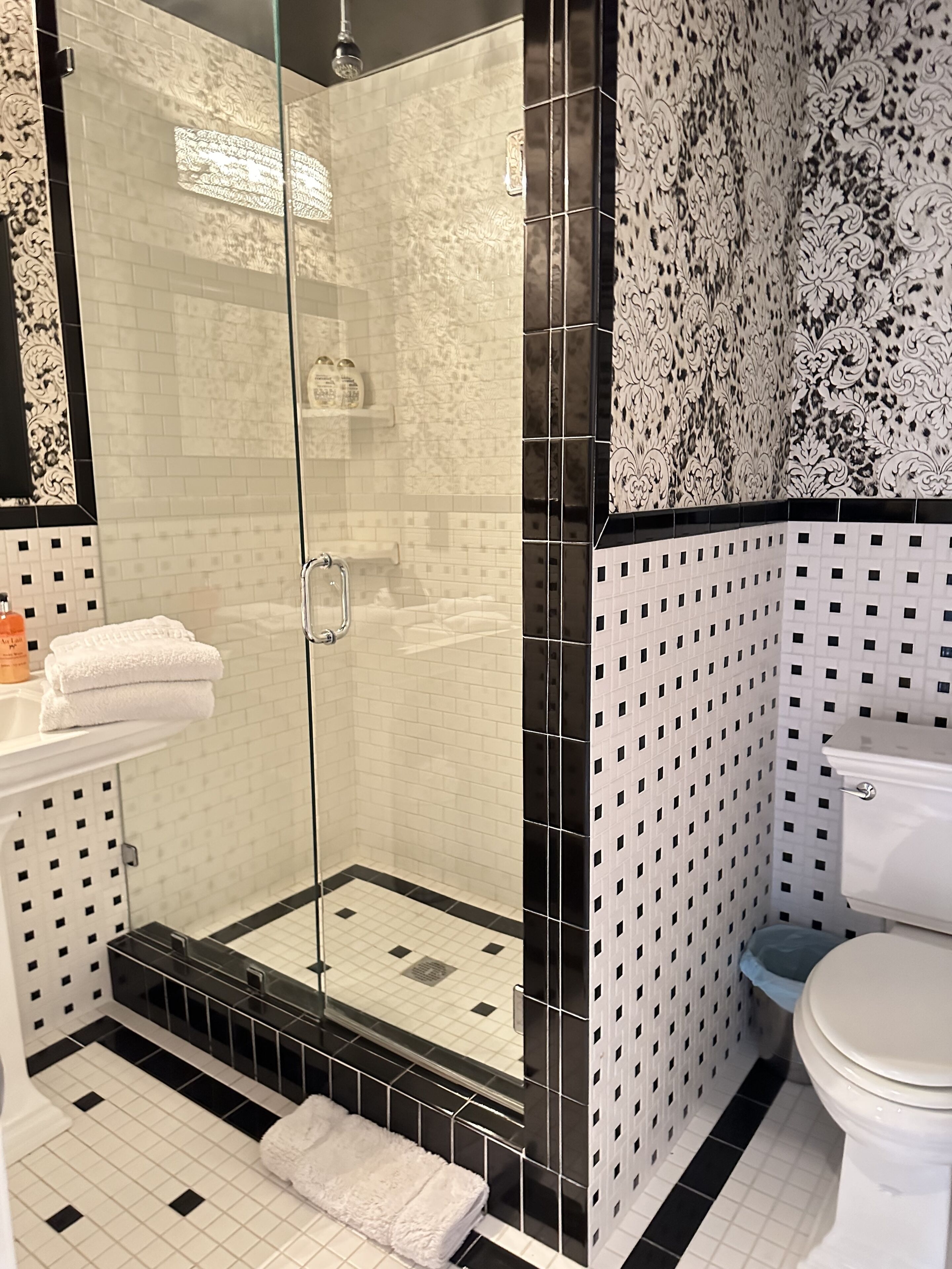 A bathroom with a glass-enclosed shower, white tiled walls, a toilet, and a sink with a mirror.