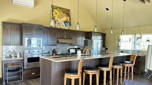 Una cocina moderna con armarios de madera oscura, electrodomésticos de acero inoxidable, una isla grande con taburetes altos e iluminación colgante.