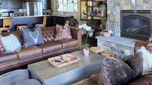 Un salón acogedor con chimenea de piedra, sofá de cuero y cocina al fondo.