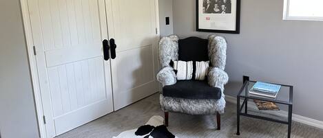 A room with a white wardrobe, a fur chair, a framed picture, and a glass table with books.