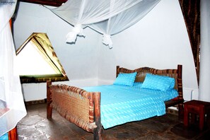 A bedroom with a bed, a small wooden stool, and a window with a curtain.