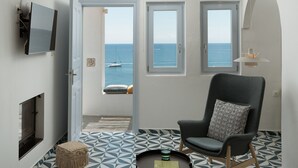 A modern living room with a view of the sea, a fireplace, and a large armchair. - Le Grand Blue Villa Santorini (Santorini)