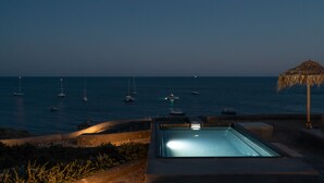 A pool area with a view of the sea and boats at dusk. - Le Grand Blue Villa Santorini (Santorini)