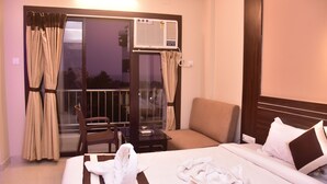 Quarto de hotel com cama, sofá, cadeira, mesa pequena e janela com cortinas.