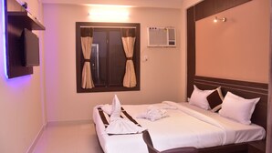 Quarto de hotel com cama, televisão fixada na parede, aparelho de ar condicionado e janela com cortinas.