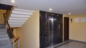 Um elevador moderno com acabamento em mármore, escada com corrimãos de madeira e um telefone fixado na parede.