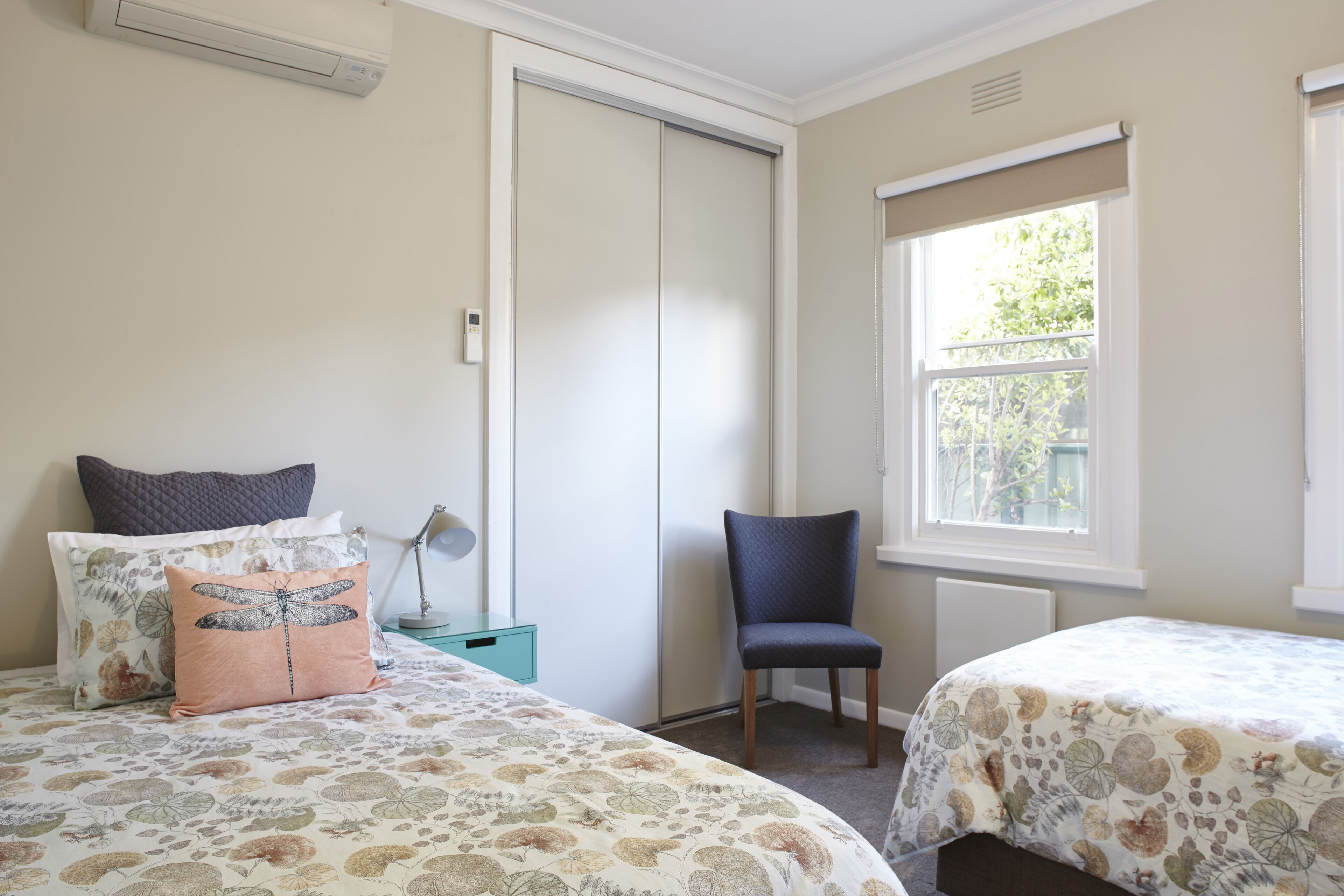 A bedroom with two beds, a chair, a wardrobe, and a window.