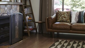 A living room with a fireplace, a sofa with cushions, a wooden ladder, and a large window with curtains. - Cuballa - Just a few minutes flat  walk to town & the river .Modern clean house (Bright)