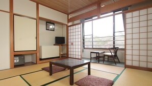 A traditional Japanese room with tatami flooring, a low table, a TV on a shelf, and a view through a shoji screen. - Kokumin Shukusha Enasansou (Ena)