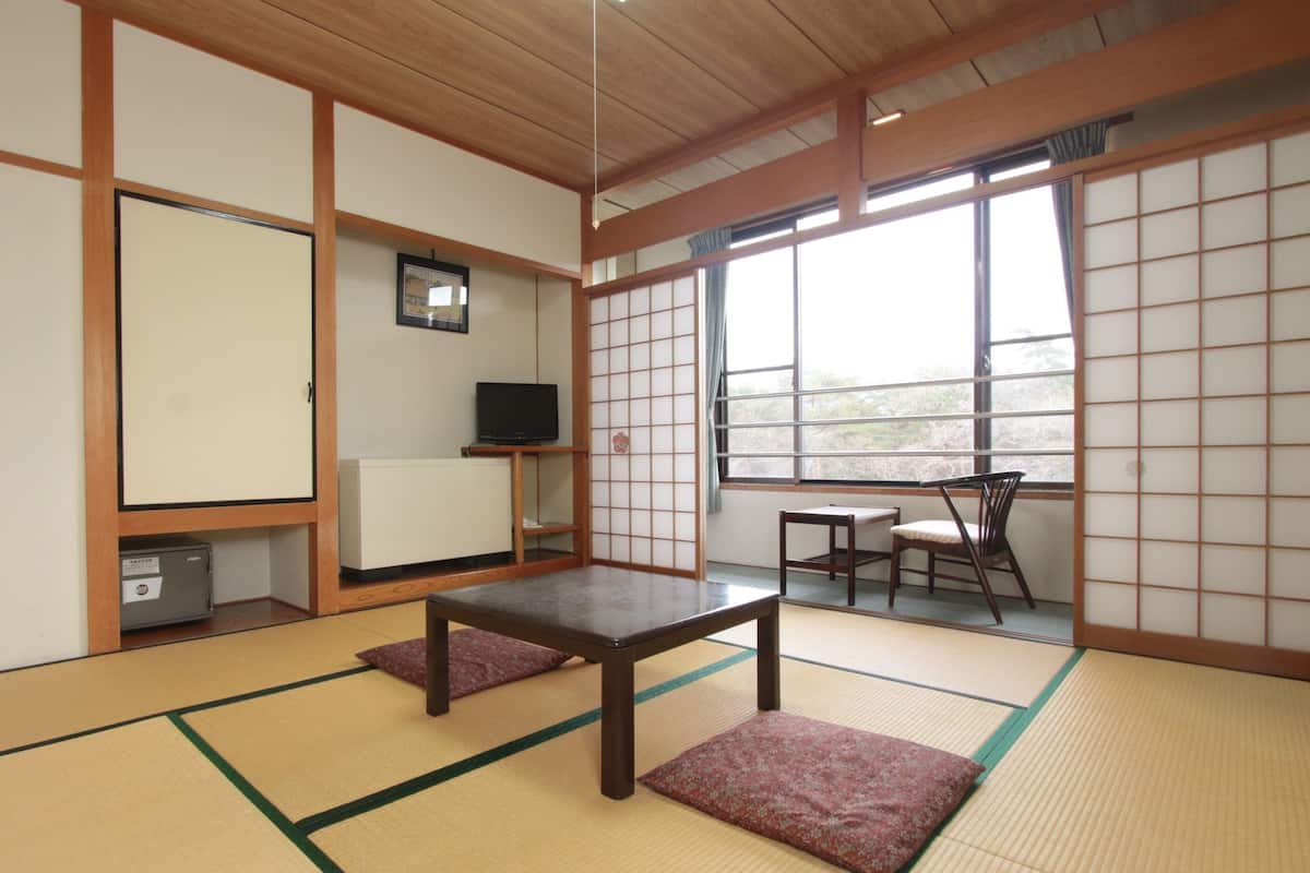 A traditional Japanese room with tatami flooring, a low table, a TV on a shelf, and a view through a shoji screen.