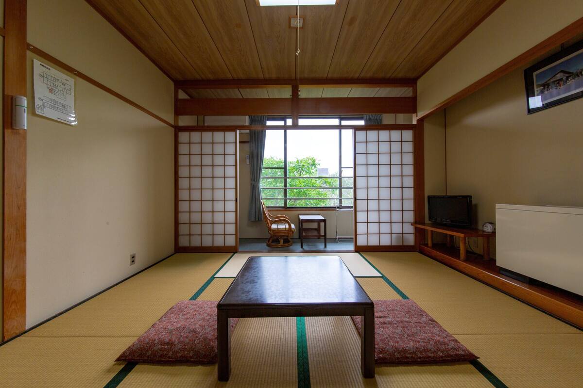 A traditional Japanese room with tatami flooring, a low table, a television, and sliding doors.