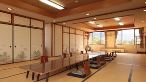 A conference room with a long table, chairs, tatami mats, sliding doors with artwork, and a view of the outdoors. - Kokumin Shukusha Enasansou (Ena)