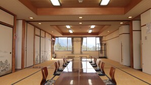 A conference room with a long table, chairs, and a view of mountains through large windows. - Kokumin Shukusha Enasansou (Ena)