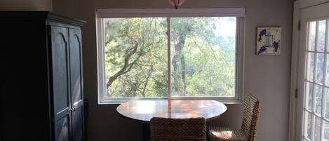 A dining area with a round table and two wicker chairs, a dark wooden cabinet, and a window with a view of trees.