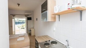 A compact kitchenette with a stove, sink, and a small shelf with kitchenware.