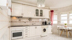 A kitchen with white cabinets, a washing machine, a coffee maker, and a dining area with a table and chairs.