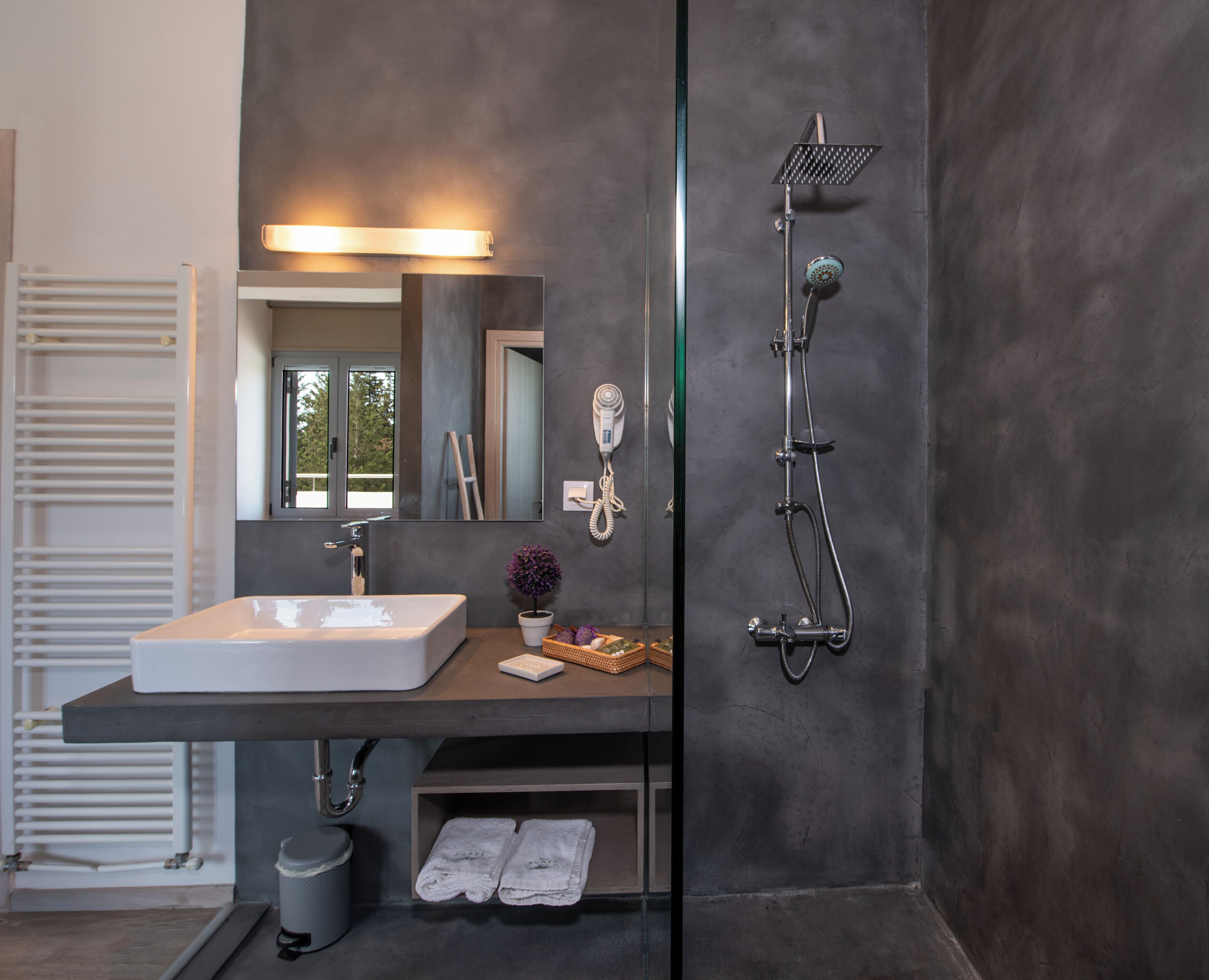 Une salle de bain moderne avec un grand miroir, un lavabo blanc, une douchette à main et un porte-serviettes.