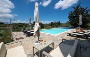 A poolside area with lounge chairs, umbrellas, and a table with drinks.