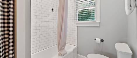 Een badkamer met een witte badkuip, een toilet en een raam met zonwering.