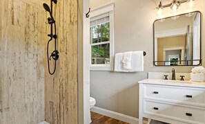 Un baño con ducha, inodoro, tocador y ventana con vistas a árboles.