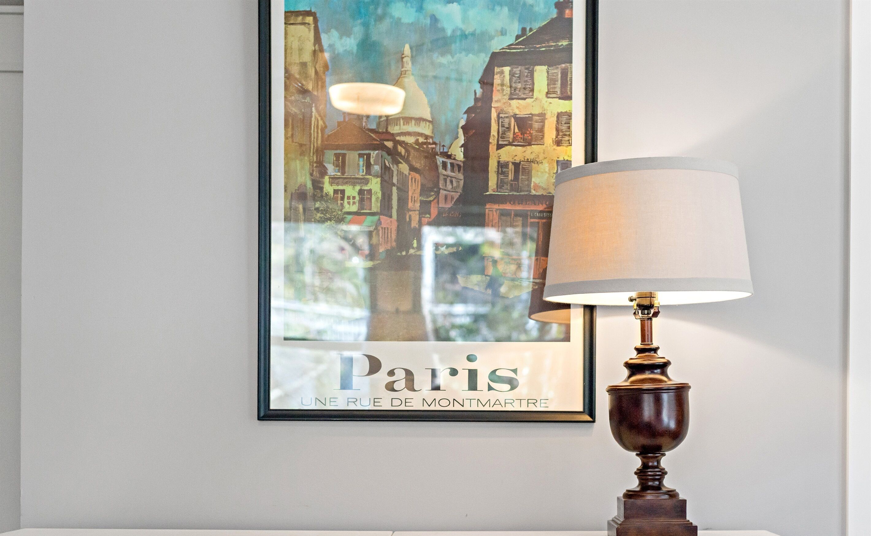 Ein gerahmtes Poster von Paris mit einer Lampe im Vordergrund.