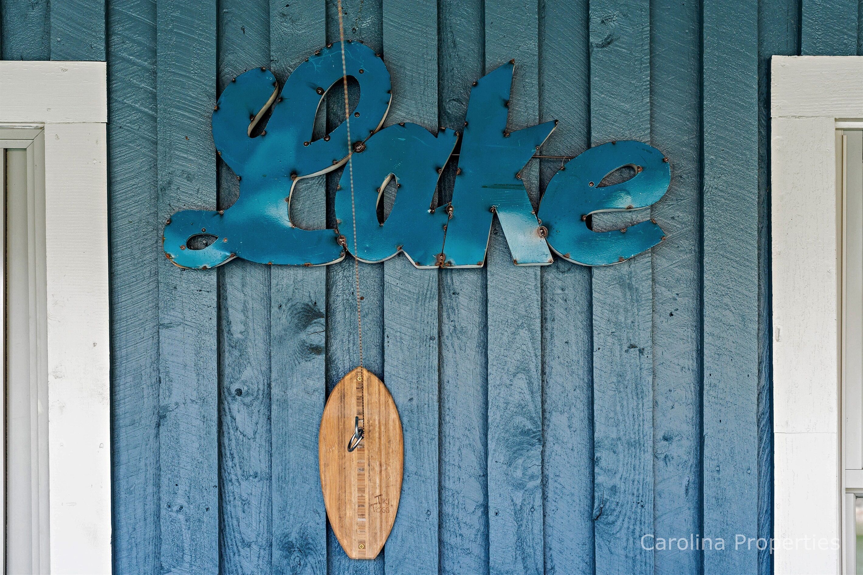 A wooden wall with the word "Lake" in blue letters and a wooden surfboard.