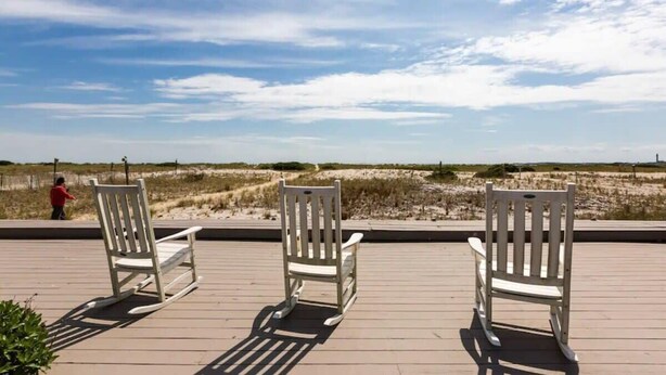 Three rocking chairs on a wooden deck overlooking a beach with sand dunes and a clear sky. - Peaceful Condo for Cozy Cape Getaway (Provincetown)