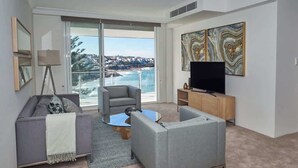 A modern living room with a sofa, armchair, coffee table, and a flat-screen TV. - Ocean View Apartment with a Stroll to Bronte Beach (Bronte)