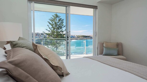 A bedroom with a large bed, a chair, a view of the sea, and a balcony. - Ocean View Apartment with a Stroll to Bronte Beach (Bronte)