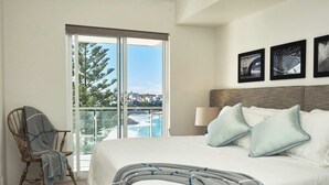 A hotel room with a bed, a chair, a balcony with a view of a bridge and cityscape, and three framed pictures on the wall. - Ocean View Apartment with a Stroll to Bronte Beach (Bronte)