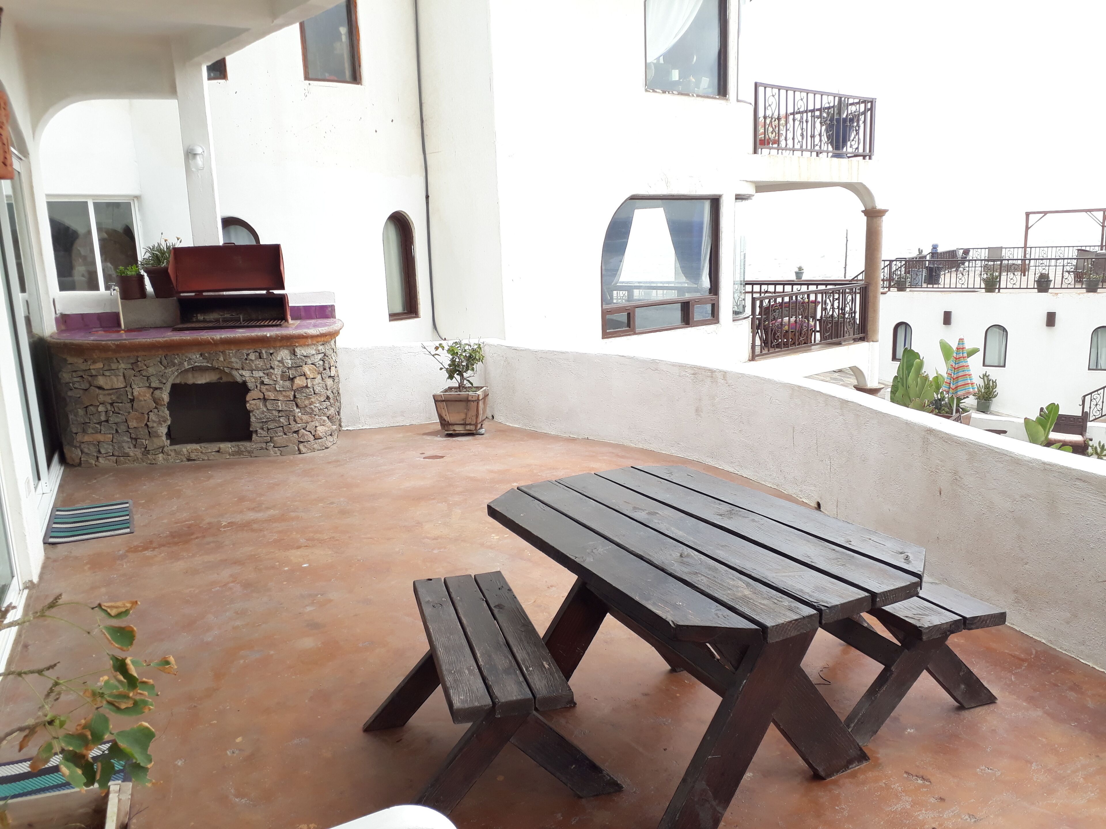 An outdoor patio with a wooden table and benches, a stone fireplace, and potted plants.