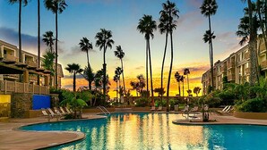 A resort pool area with palm trees and a sunset view.