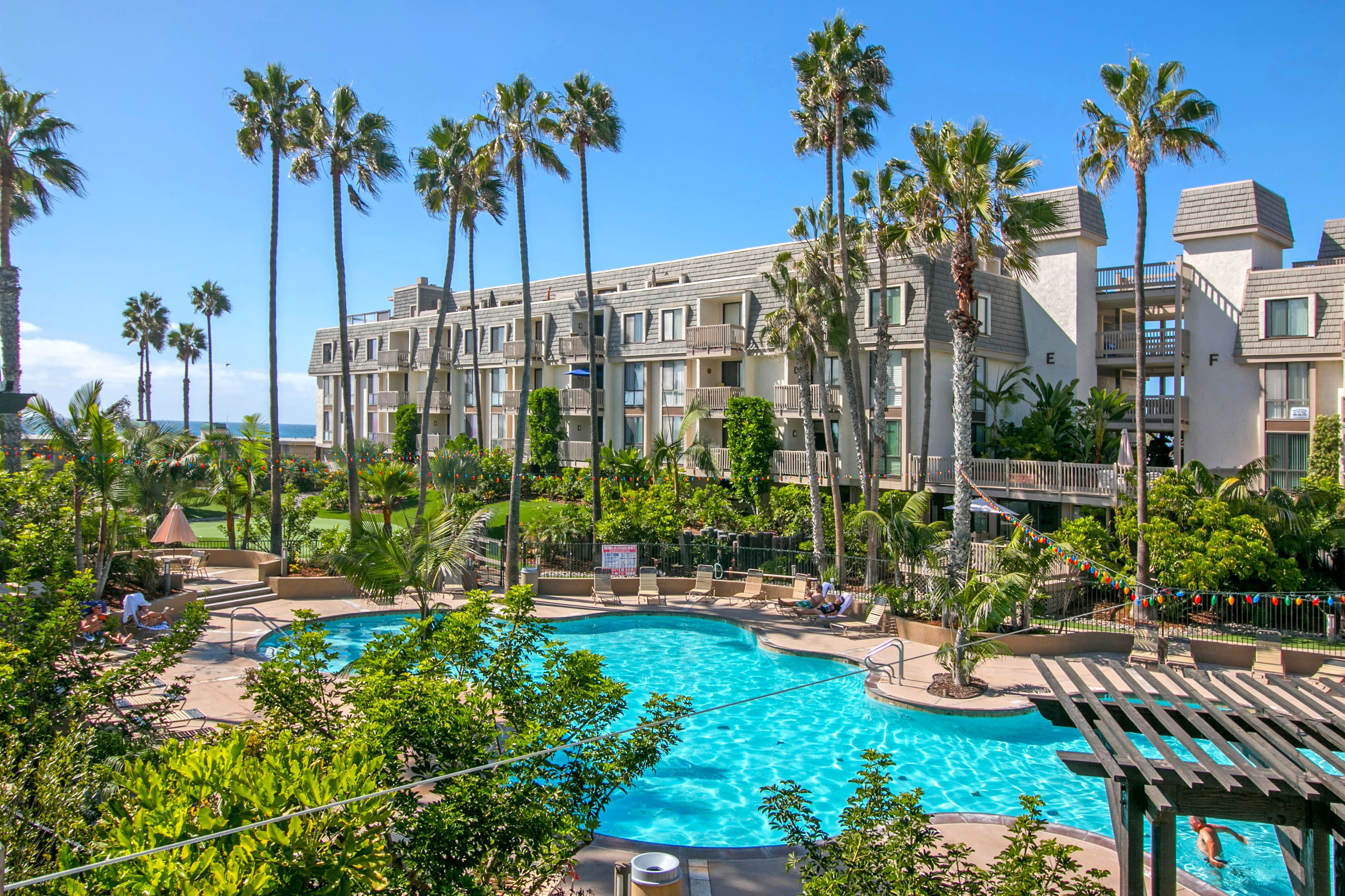 A hotel with a swimming pool surrounded by palm trees and a view of the ocean.