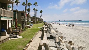 A beachfront hotel with a patio area, palm trees, and a view of the ocean.