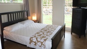Quarto com cama, penteadeira, televisão e janela com cortinas.