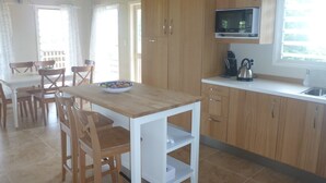 Cozinha moderna com armários de madeira, bancada branca e área de refeições com mesa e cadeiras.